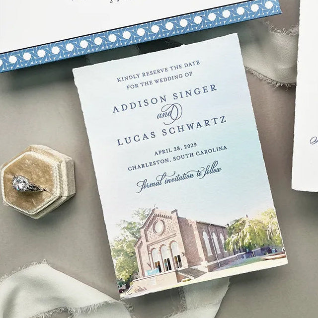 Save the Date with a church illustration, ring, and ribbon on a gray surface.