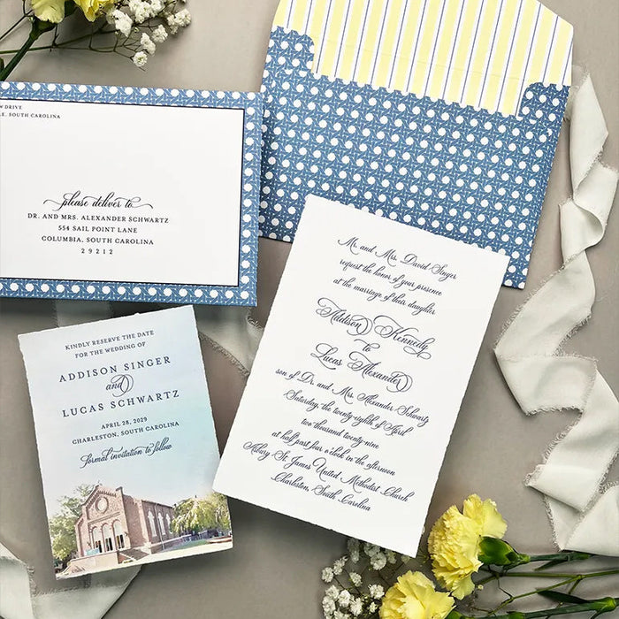 Wedding invitation set with blue and white patterned envelope, card, and matching Save the Date card on a gray surface with yellow flowers.