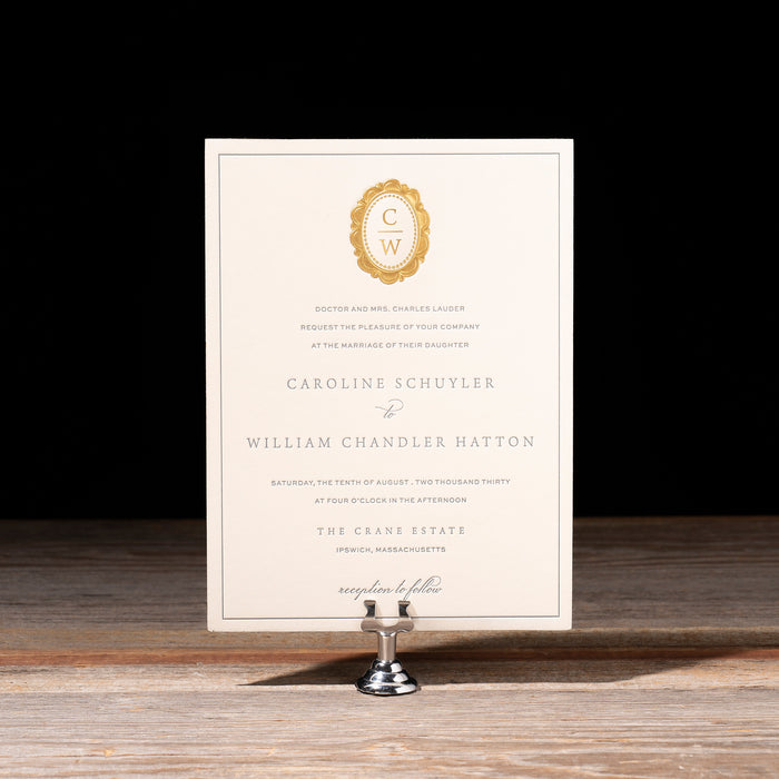 Charmain Invitation card with gold emblem on a stand against a black background