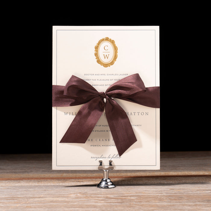 Charmain Invitation card with a brown bow on a stand against a black background
