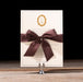 Charmain Invitation card with a brown bow on a stand against a black background