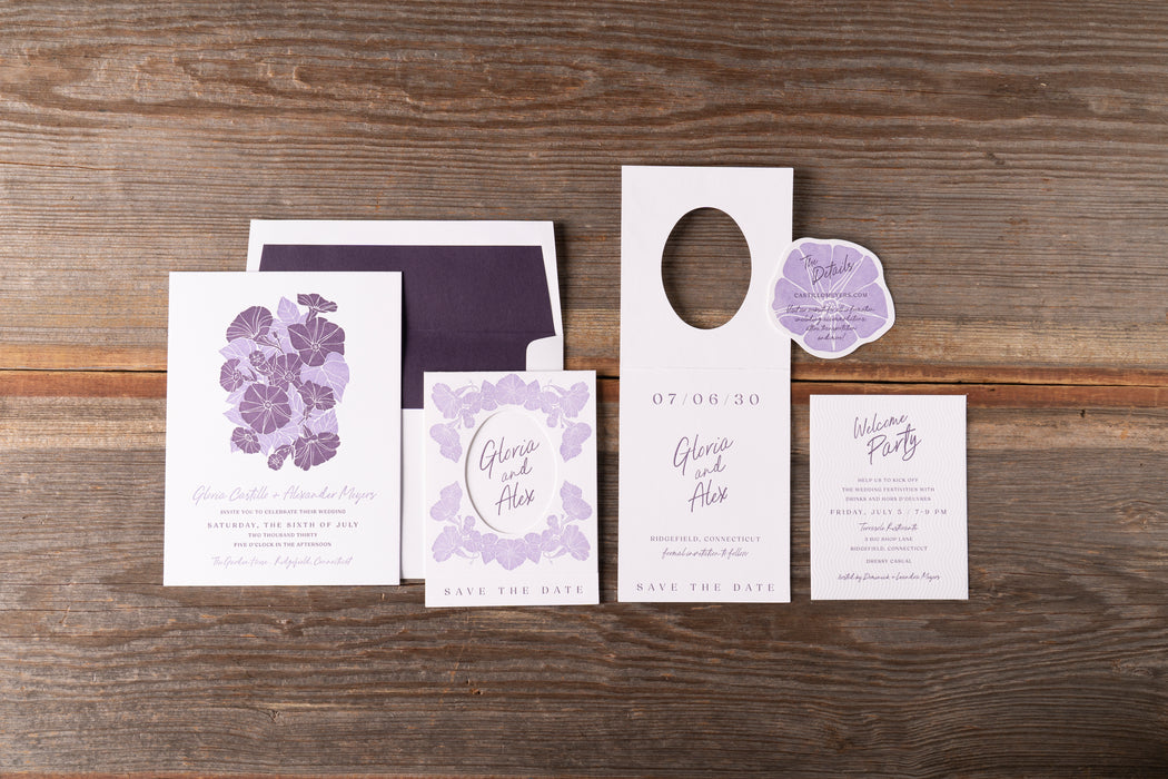 Gloria wedding invitation set with purple floral designs on a wooden surface