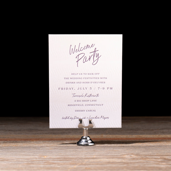 Gloria suite Welcome party invitation card on a stand with a dark background