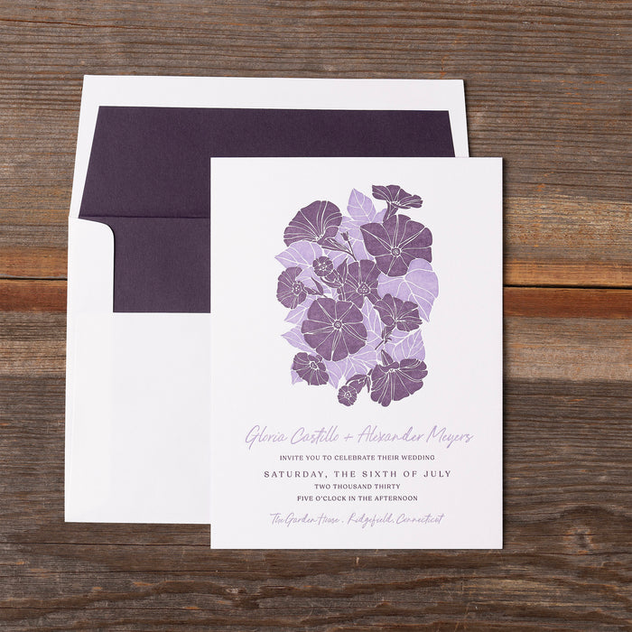 Gloria Wedding invitation with purple floral design on a wooden surface