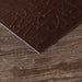 Edgepainted corner detail of dark brown embossed text invitation on a wooden surface