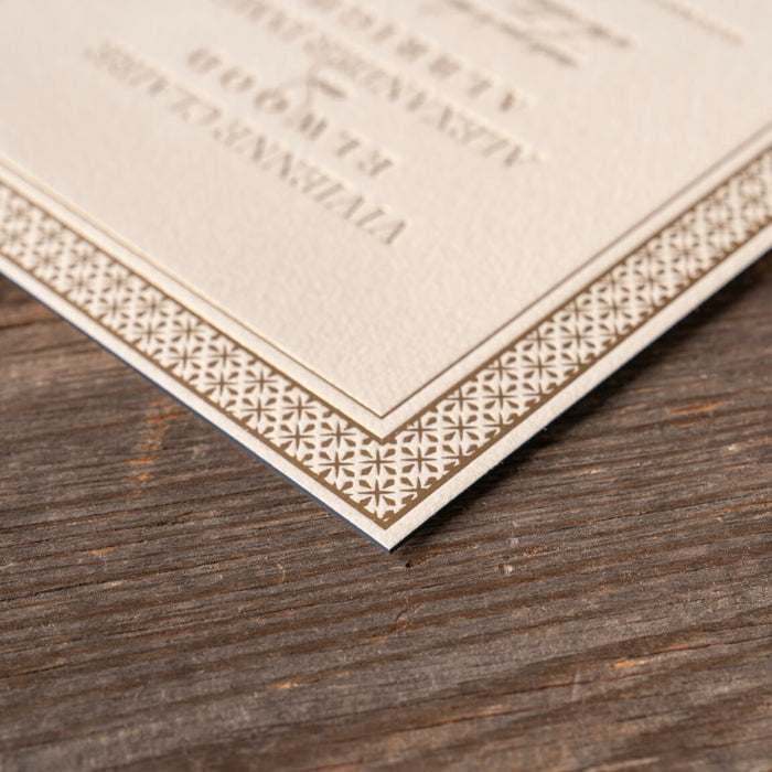 Corner of a decoratively framed wedding invitation with text on a wooden surface