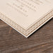 Corner of a decoratively framed wedding invitation with text on a wooden surface