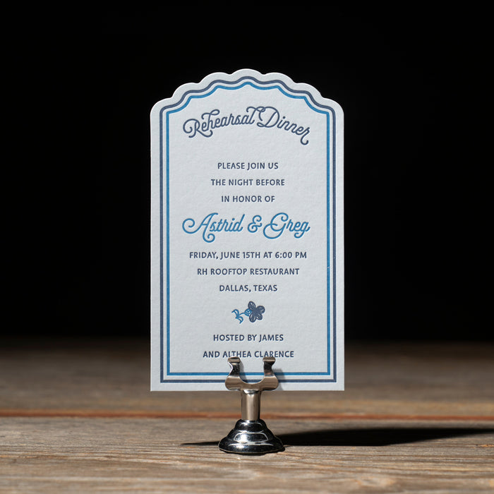 Astrid Rehearsal Dinner card on a stand with a dark background