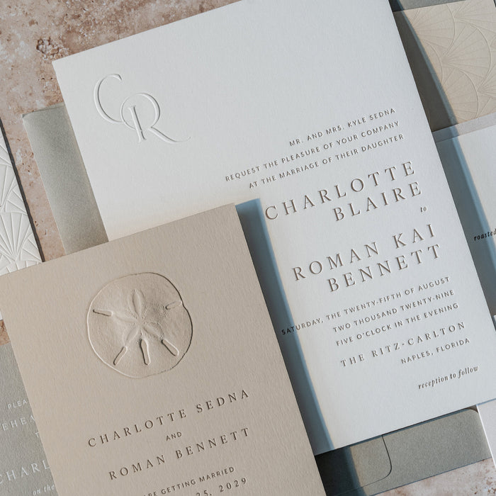 Collection of elegant wedding invitation cards from the Sedna Suite with embossed designs on a textured surface.