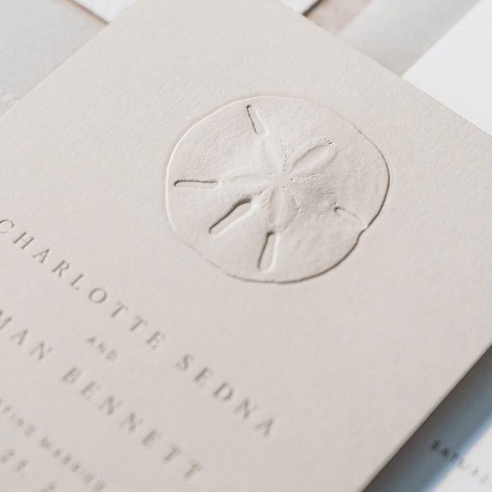 Beige save the date card with sand dollar design and text on a white surface