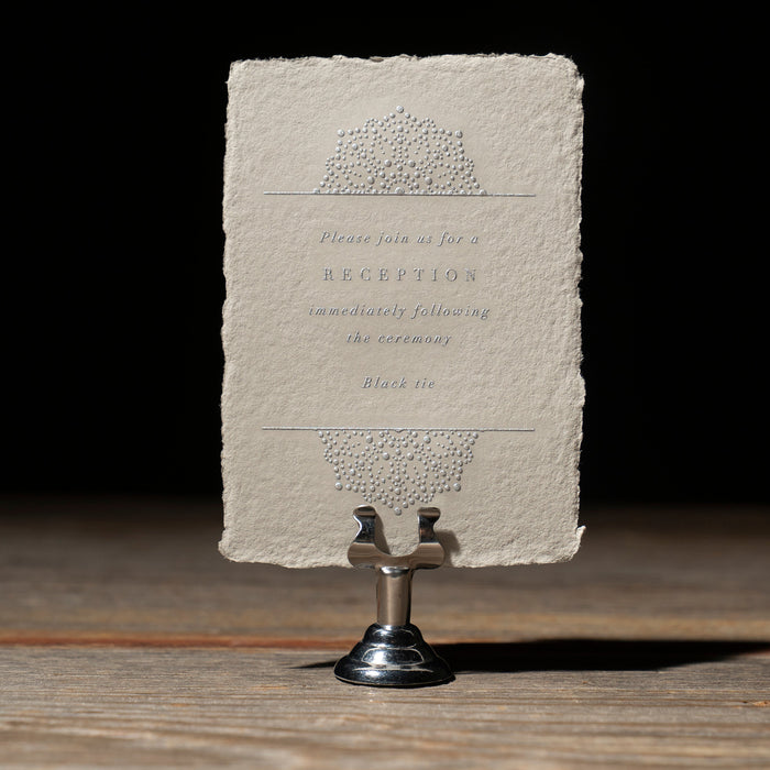 Vintage-style wedding invitation reception card on a stand against a dark background