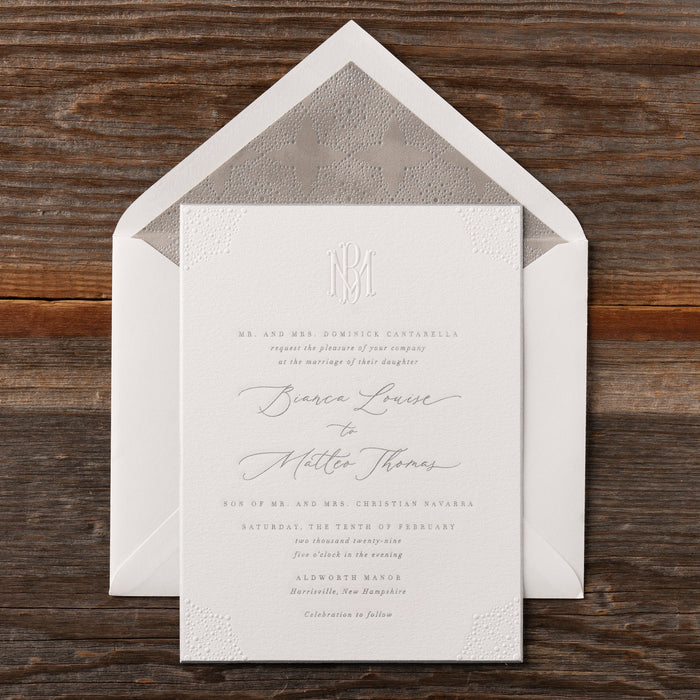 White Bianca wedding invitation with monogram and text on a wooden surface