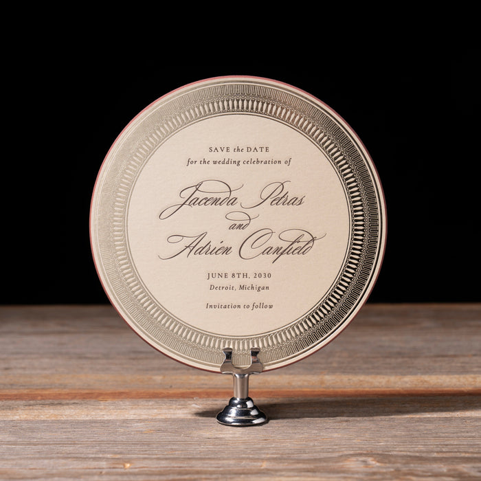 Canfield round shaped save the date card with gold border on stand against dark background