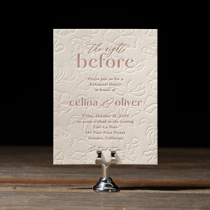 Celina rehearsal dinner card with intricate text on a wooden stand against a dark background
