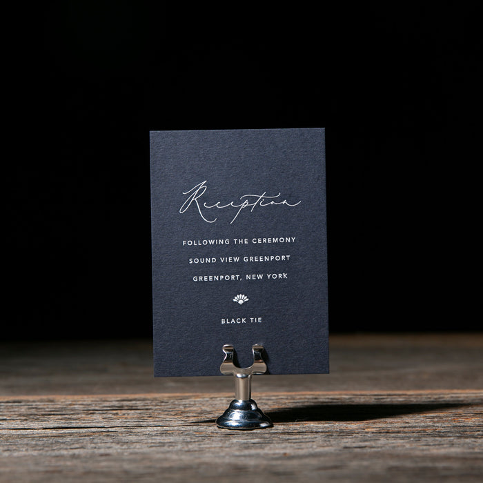 Navy blue reception card on a stand with a dark background