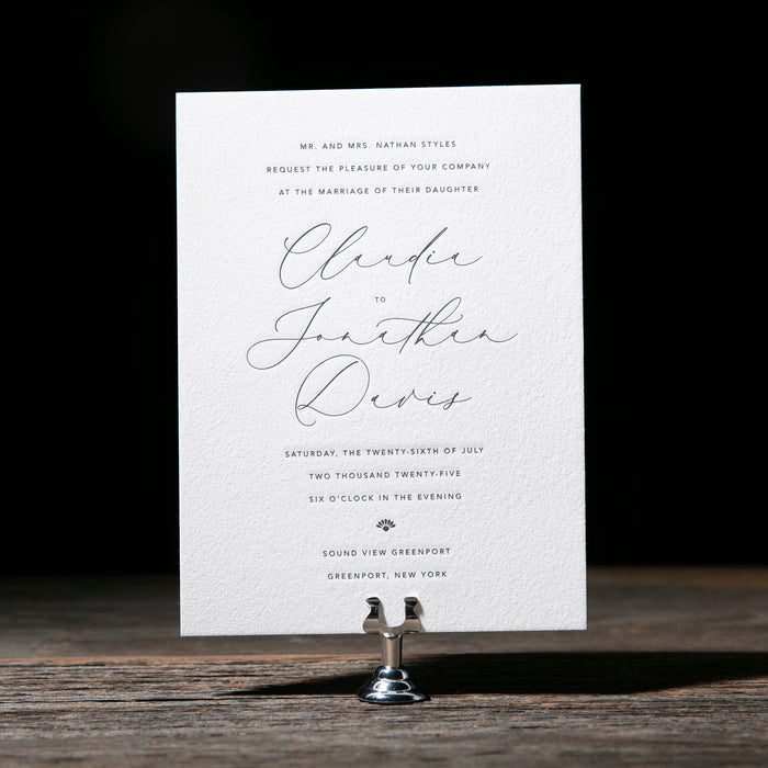 White wedding invitation card on a wooden stand against a dark background