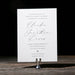 White wedding invitation card on a wooden stand against a dark background