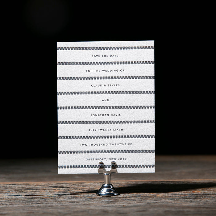 Blue and white striped 'Save the Date' card on a wooden stand with a dark background