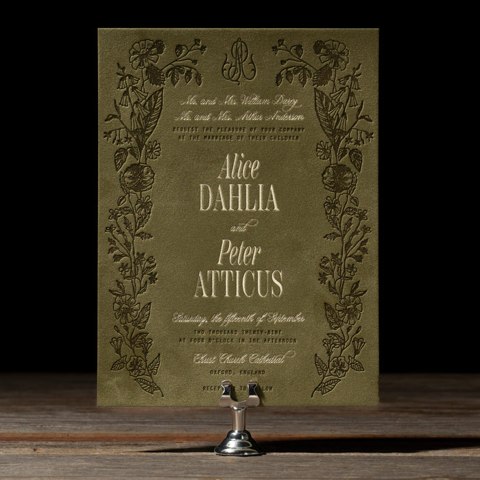 Decorative Darcy wedding invitation with intricate designs on a wooden stand against a dark background