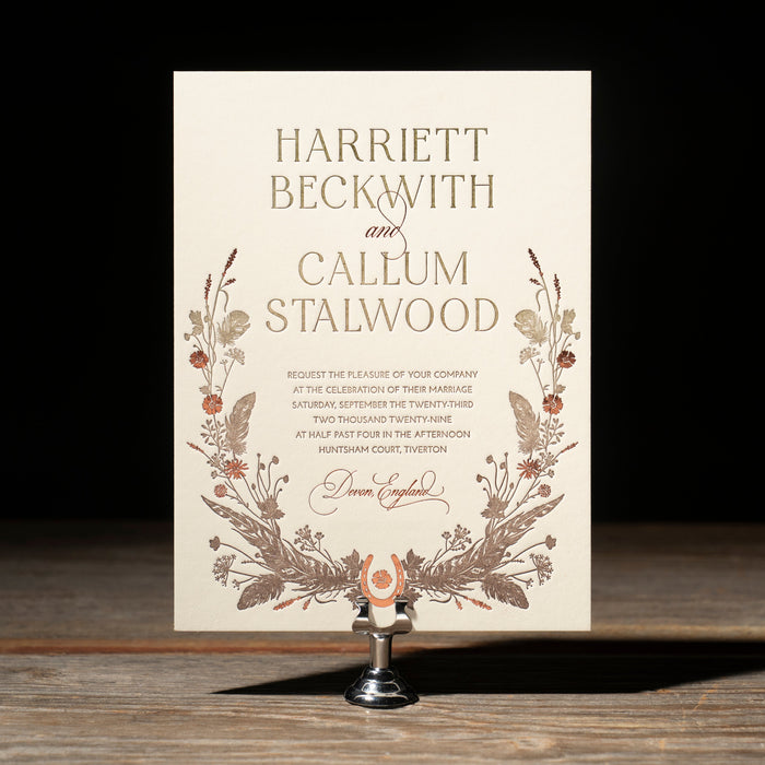 Devonshire wedding invitation card with floral design on a stand against a dark background