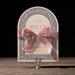 Decorative wedding invitation with a pink bow on a stand against a black background