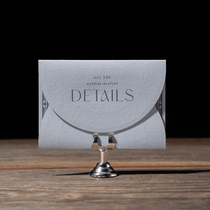 Card with 'All the wedding weekend details' text on a stand against a dark background