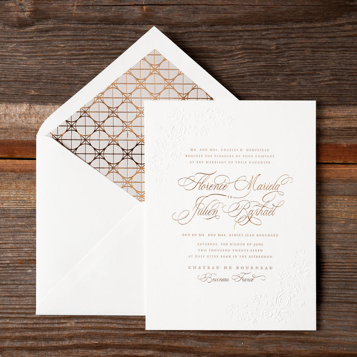 White invitation card with bronze text on a wooden surface