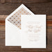 White invitation card with bronze text on a wooden surface