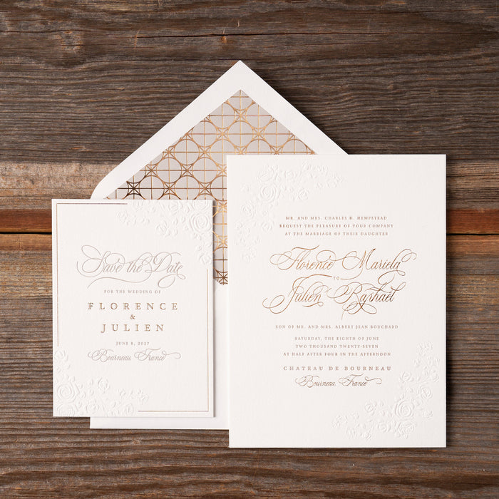 White wedding invitation with bronze text on a wooden surface