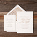 White wedding invitation with bronze text on a wooden surface