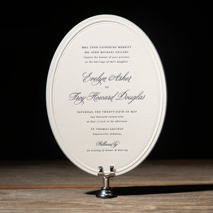 Elegant Gellert oval wedding invitation on a stand with a dark background