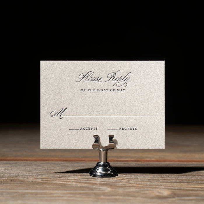 Vintage-style wedding reply card on a stand against a dark background