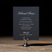 Dark blue rehearsal dinner card on a stand with a dark background