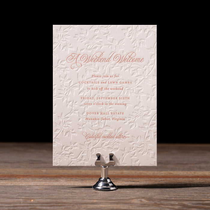 Wedding welcome party card with textured surface and text on a wooden stand against a dark background