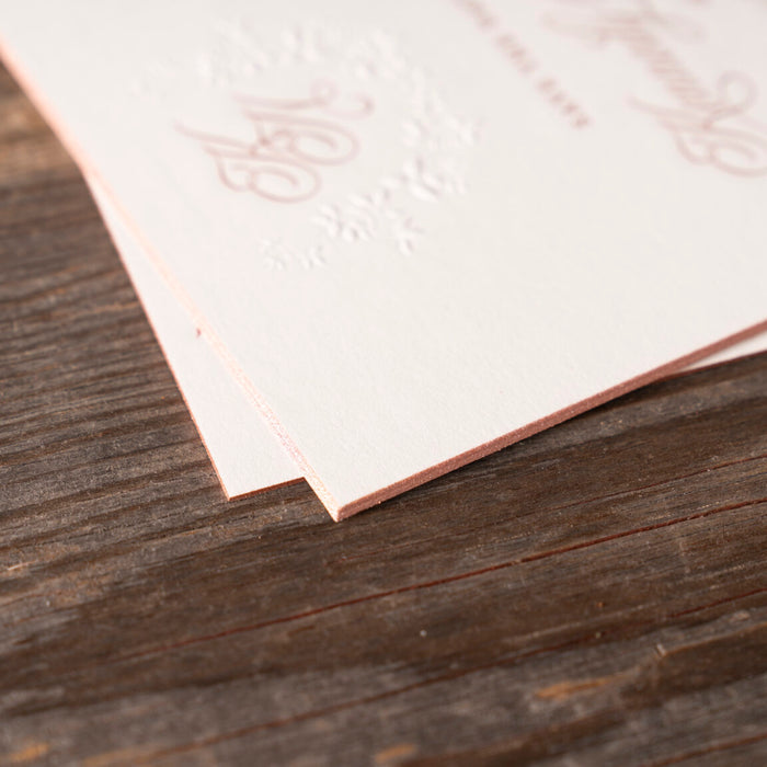 White paper with engraved text and rose gold edgepaint on a wooden surface