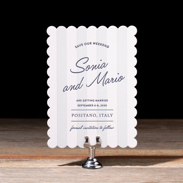 White scalloped edge card with navy text on a wooden stand against a dark background