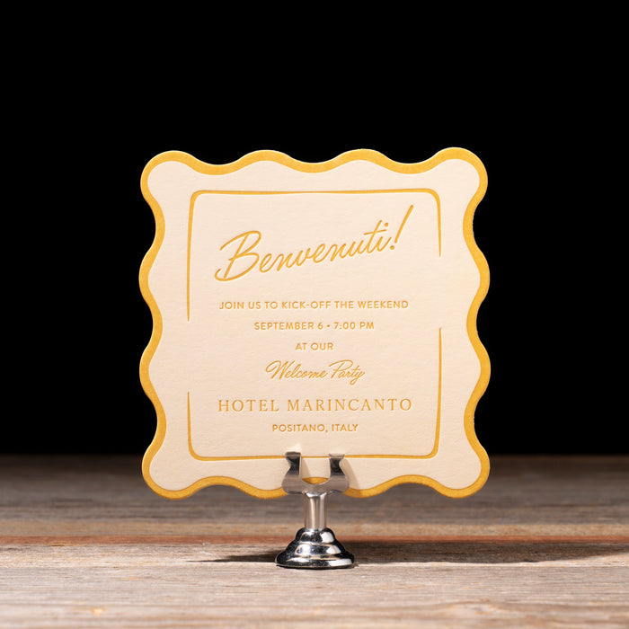 Welcome Party Invitation card with decorative border on a stand against a dark background
