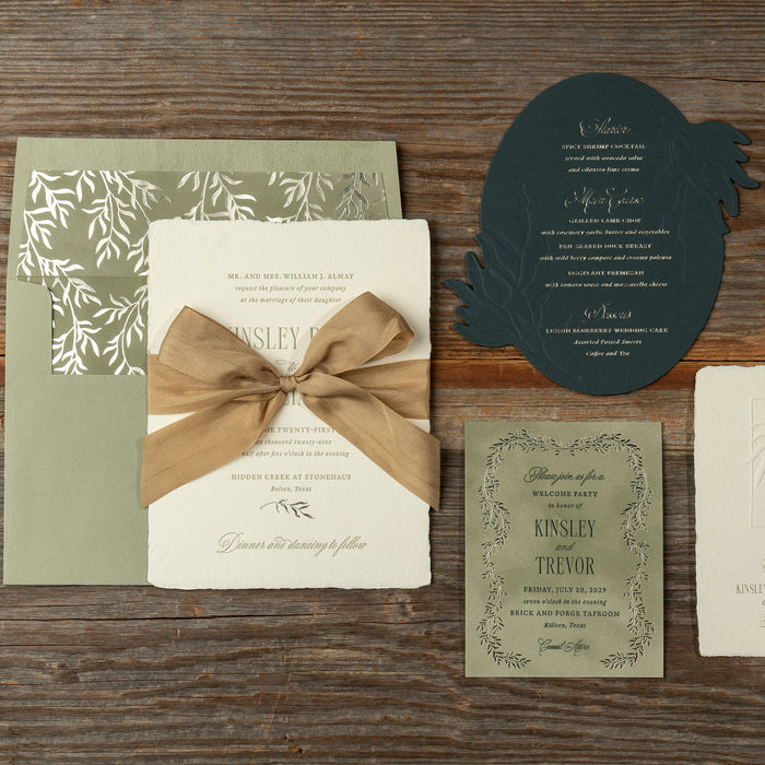 Kinsley wedding invitation set with green and beige colors on a wooden surface
