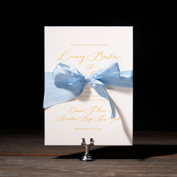 Lainey wedding invitation card with a blue ribbon on a dark background