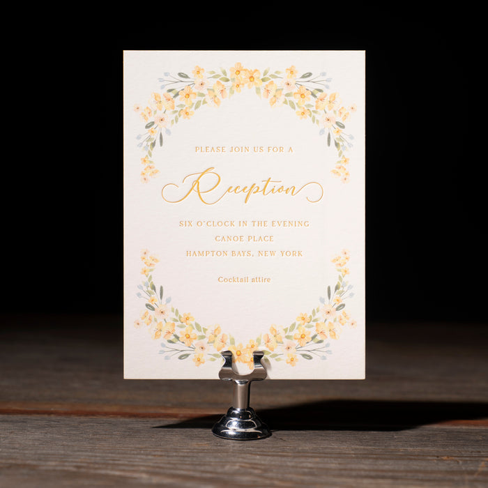 Wedding reception card with floral design on a stand against a dark background