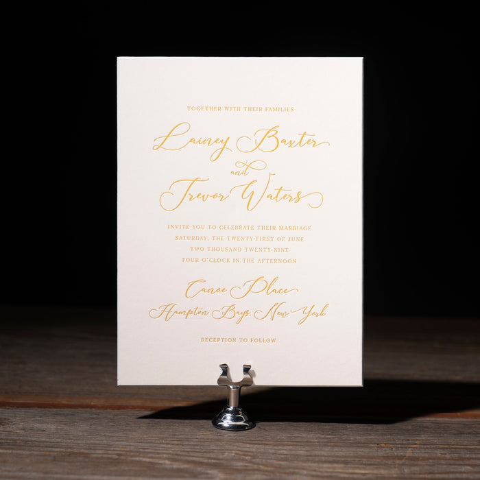 Lainey wedding invitation card on a stand with gold text against a dark background