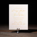 Lainey wedding invitation card on a stand with gold text against a dark background