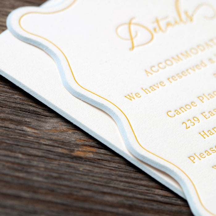Close-up of a wedding invitation card with gold text on a wooden surface