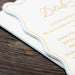 Close-up of a wedding invitation card with gold text on a wooden surface