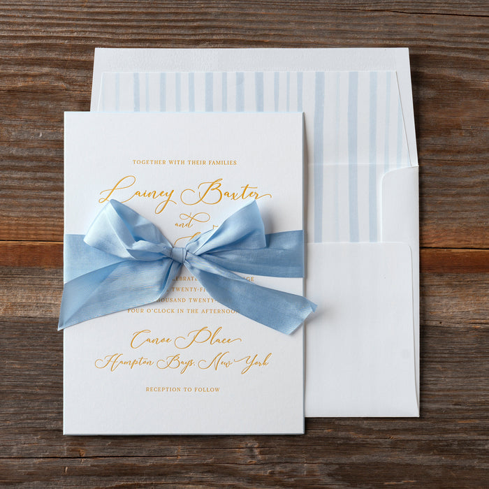 Lainey wedding invitation with blue bow on a wooden surface