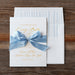 Lainey wedding invitation with blue bow on a wooden surface