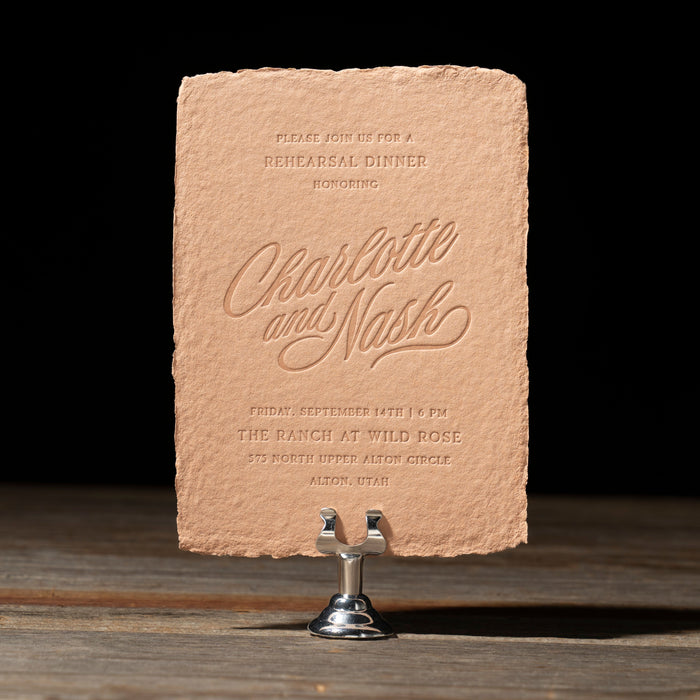 Nash textured Rehearsal Dinner card with letterpress text on a stand against a black background