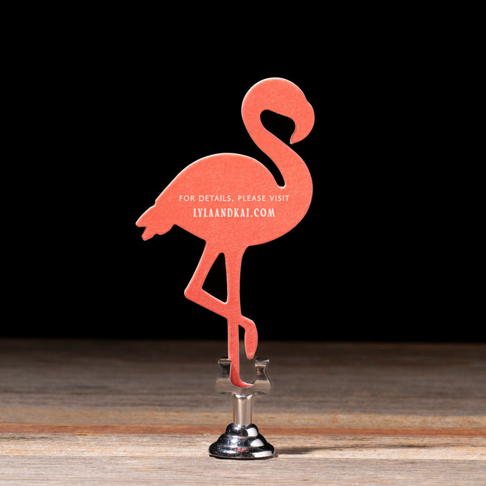 Pink flamingo-shaped website card on a wooden surface with a dark background