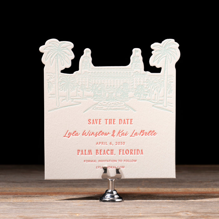 White 'Save the Date' card with hot pink text on a stand against a black background