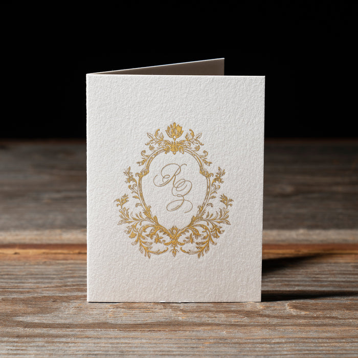 Rhea folding thank you card with gold monogram design on a wooden surface